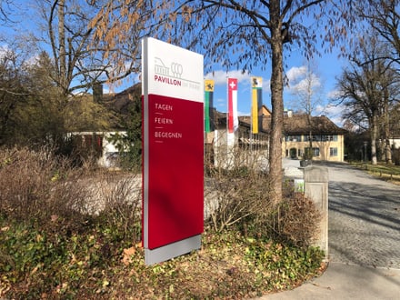 Schild des Pavillons im Park mit Flaggen im Hintergrund.