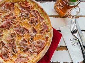 Pizza mit Schinken und Glas Eistee auf Tisch.