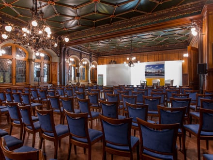 Historischer Konferenzraum mit Stuhlreihen und Bühne.