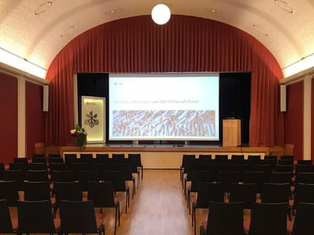 Leerer Konferenzsaal mit Bühne und Projektorleinwand.