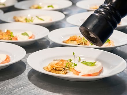Hand würzt mehrere Teller Pasta mit Pfeffer.