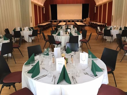 Festlich gedeckter Speisesaal mit runden Tischen und Bühne.