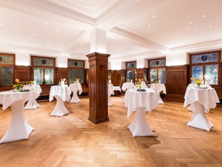 Eleganter Veranstaltungsraum mit Stehtischen und Holzvertäfelung.