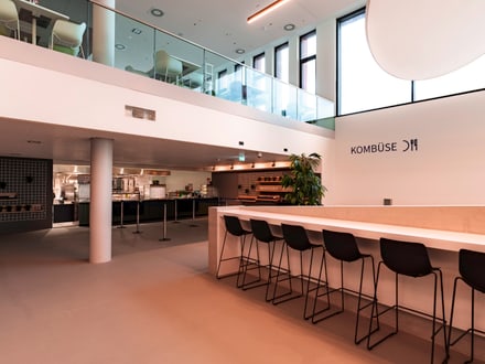 Moderne Cafeteria mit hohen Decken und Barhockern.