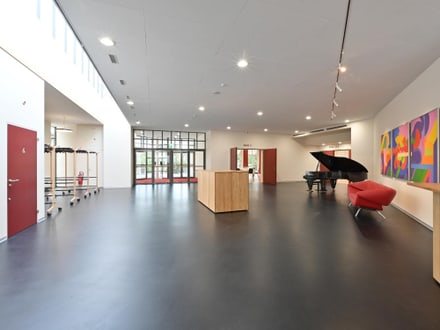 Moderner Saal mit Flügel, roten Stühlen und Kunstwerk an der Wand.