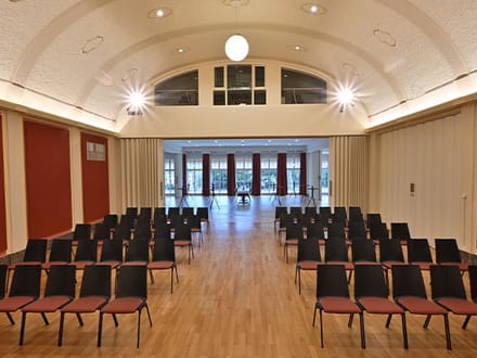 Leerer Veranstaltungsraum mit Stühlen in Reihen auf Holzboden.