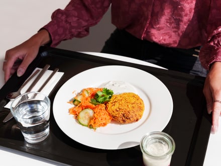 Person in rotem Oberteil mit Tablett und Essen.
