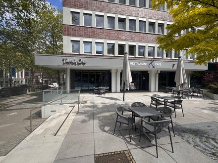 Aussenansicht eines Cafés mit Sitzgelegenheiten auf einer Terrasse.