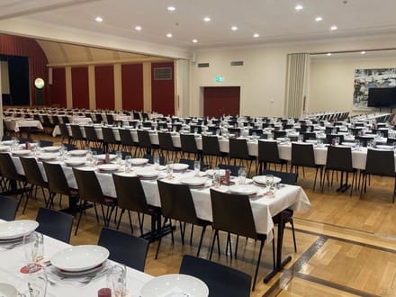 Grosser Saal mit langen gedeckten Tischen und Stühlen.