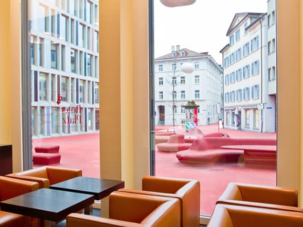 Innenansicht eines Cafés mit Blick auf moderne Gebäude und roten Platz.