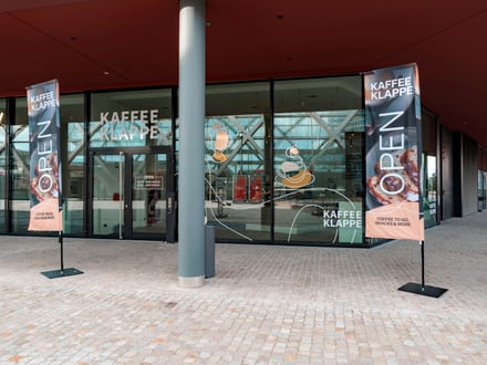 Aussenansicht eines Cafés mit Glasfront und Werbebannern.