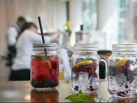 Zwei Glasgefässe mit fruchtigen Getränken auf einem Tisch, verschwommene Menschen im Hintergrund.