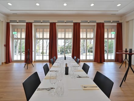 Eleganter Speisesaal mit gedecktem Tisch und roten Vorhängen.