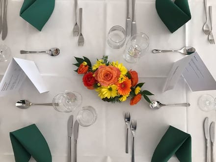 Gedeckter Tisch mit Blumengesteck und grünen Servietten.