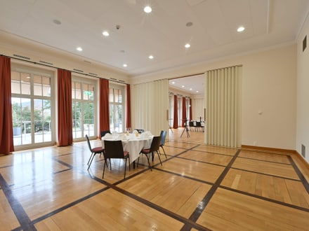 Leerer Raum mit Holzboden und eingerichtetem Tisch neben grossen Fenstern.