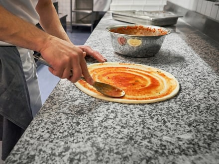 Koch verteilt Tomatensauce auf Pizzateig in Küche.