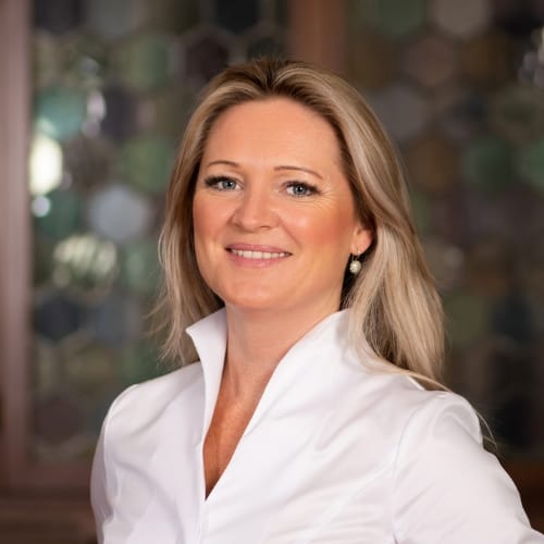 Lächelnde Person mit blonden Haaren vor unscharfem Hintergrund.