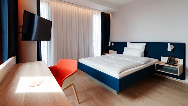 Modernes Hotelzimmer mit Bett, Tisch, Stuhl und Fernseher.