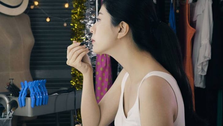 Frau trägt Lippenstift vor Spiegel auf.