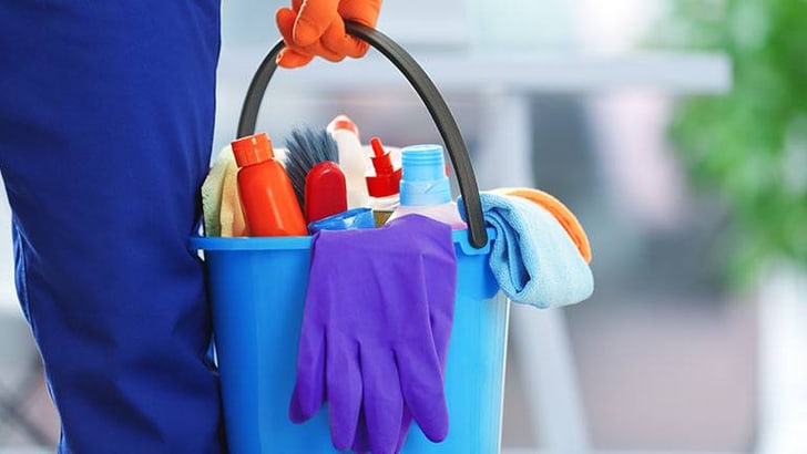 Nahaufnahme eines Eimers mit Putzmitteln und Handschuhen.