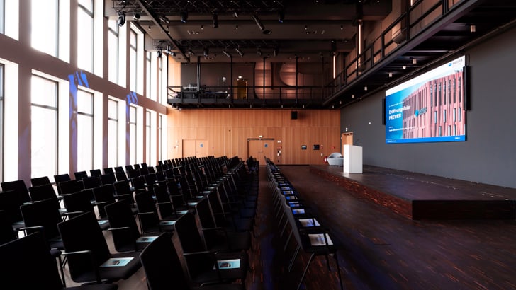 Leerer Konferenzraum mit Reihen von Stühlen und einer grossen Leinwand.