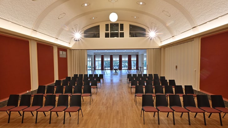 Leerer Veranstaltungsraum mit Stühlen in Reihen auf Holzboden.