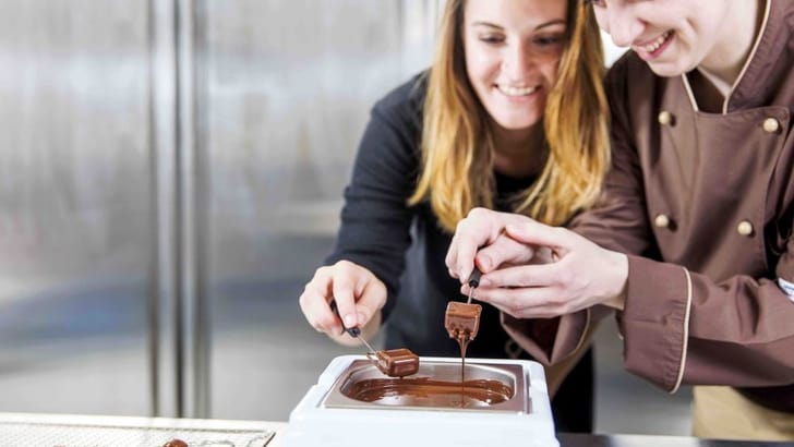 Zwei Frauen tauchen Schokolade in einem Schokoladenschmelzer ein.