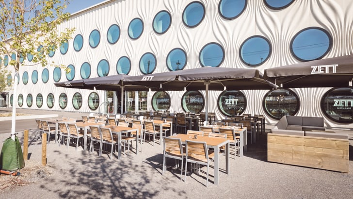 Aussenbereich eines Cafés mit runden Fenstern an der modernen Fassade.