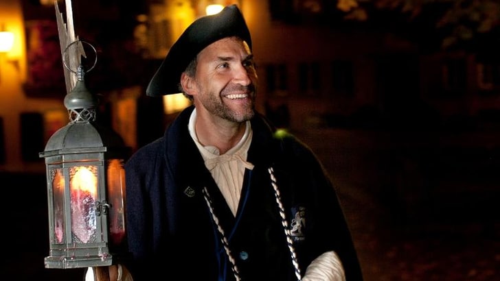 Person in historischem Kleid mit Laterne im Freien bei Nacht.