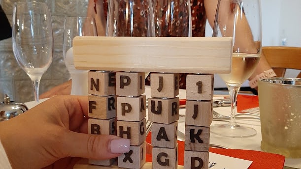 Hand mit Holzspiel auf einem Tisch mit leeren Weingläsern.