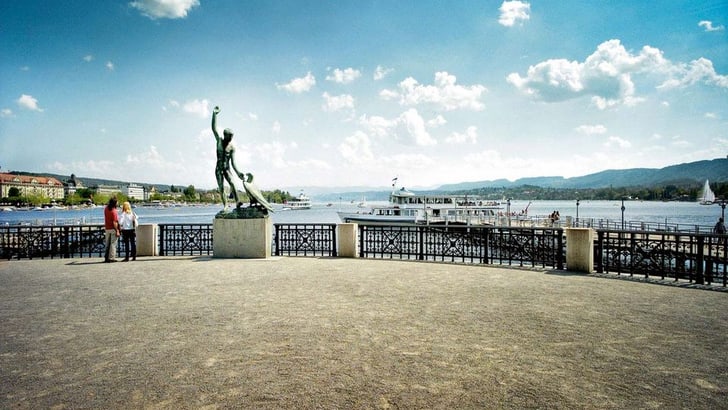 Seeblick mit Statue und Schiffen bei klarem Himmel.
