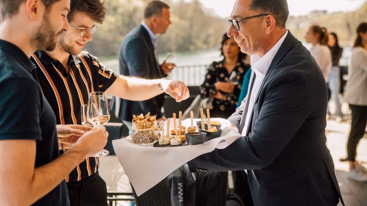 Person serviert Snacks auf einem Tablett bei einem Empfang im Freien.