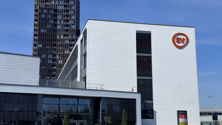 Modernes Gebäude mit Firmenlogo bei sonnigem Himmel.