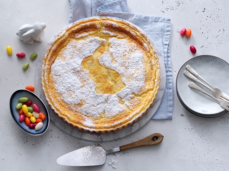 Zitronenkuchen mit Hasenmotiv, Ostereiern und Geschirr auf Tisch.