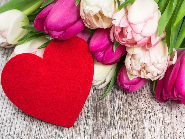 Rotes Herz neben rosa und weissen Tulpen auf Holzoberfläche.
