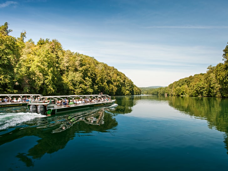 Ausflugsschiffe auf breitem Fluss mit Bäumen an beiden Ufern.