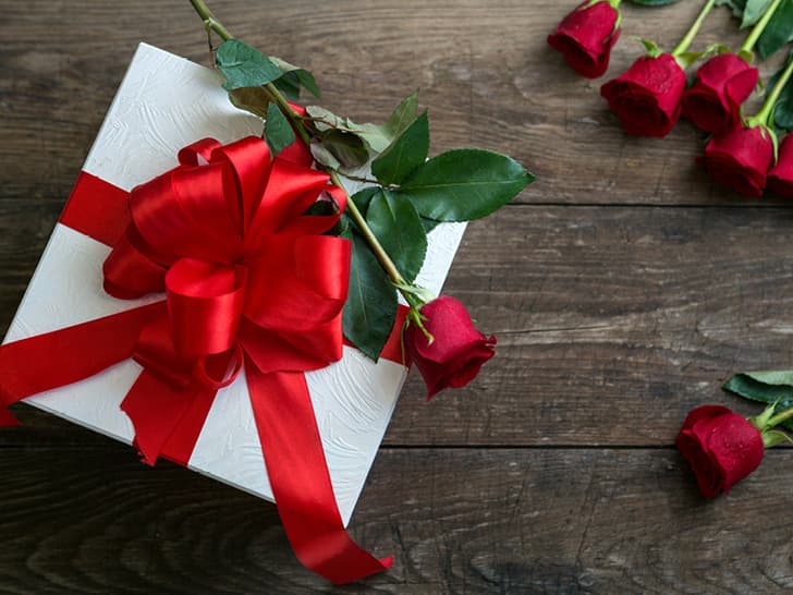 Geschenkbox mit roter Schleife und Rosen auf Holztisch.