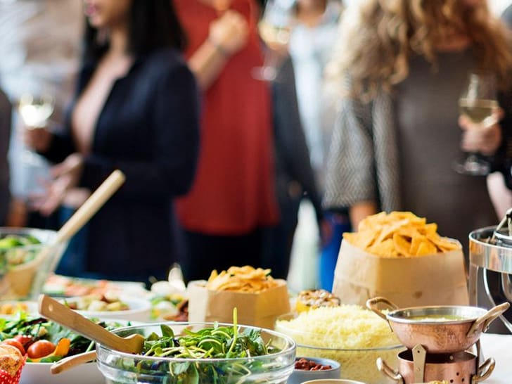 Buffet mit verschiedenen Speisen und Menschen im Hintergrund bei einer Veranstaltung.