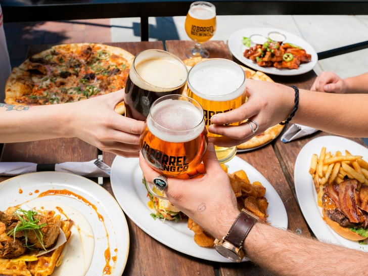 Menschen stossen mit Biergläsern an, Essen auf Tisch.