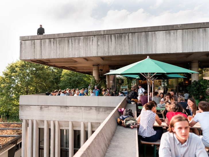 Menschen in einem Café auf einer Dachterrasse bei Sonnenschirmen.",