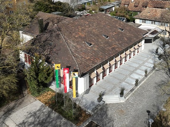 Luftaufnahme eines Gebäudes mit Flaggen davor, umgeben von Bäumen.