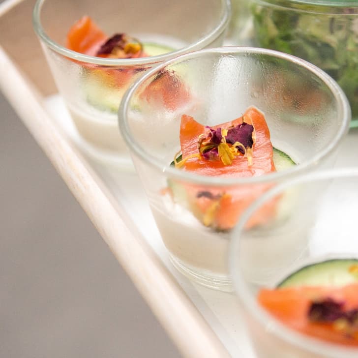 Gläser mit Lachs und essbaren Blüten auf Tablett.