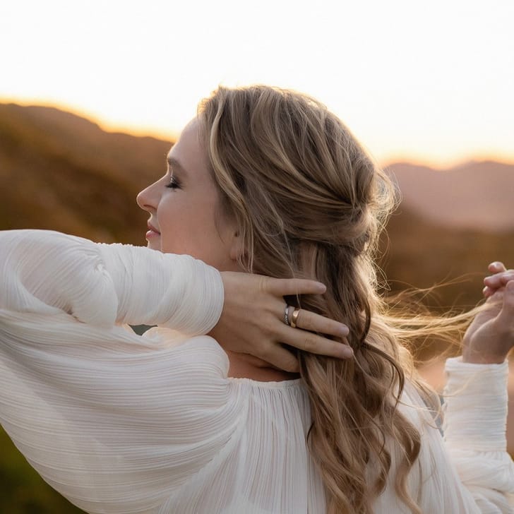 Frau in weissem Kleid vor hügeliger Landschaft.