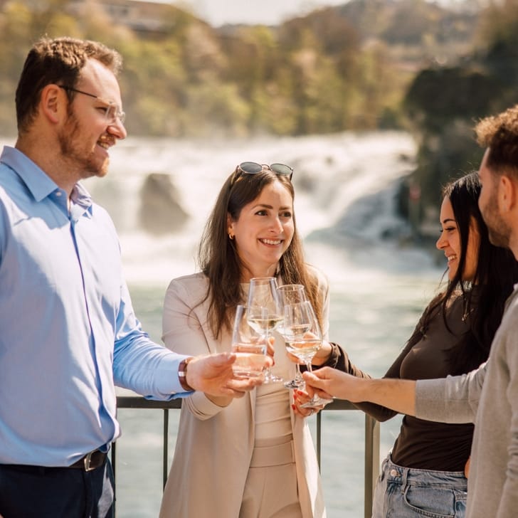 Gruppe von Menschen stösst mit Getränken vor Wasserfall an.