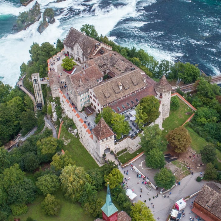 Luftbild eines Schlosses am Fluss mit Wasserfällen und einer Brücke.
