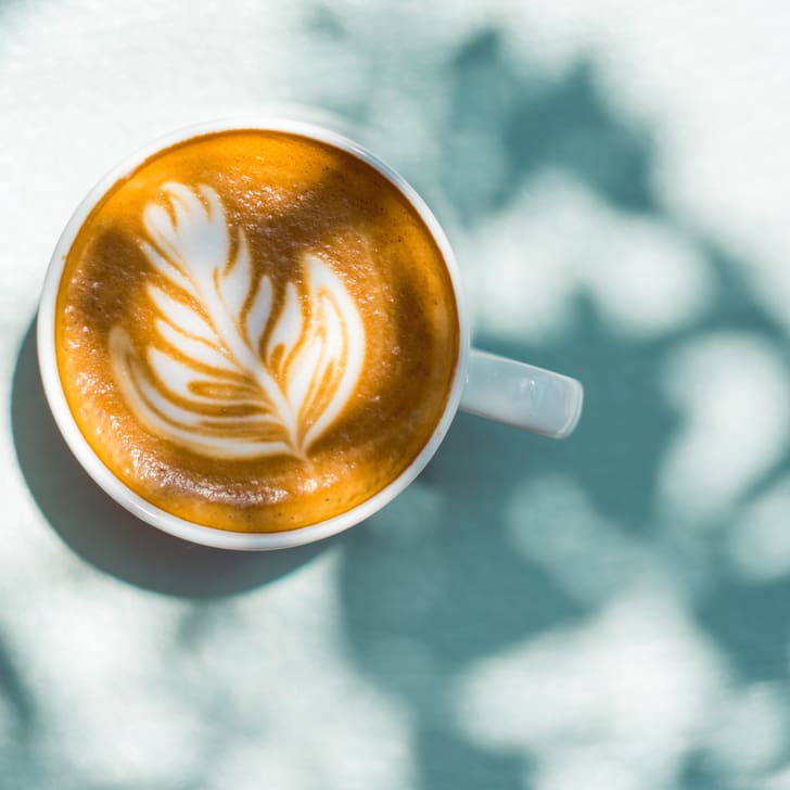 Tasse Cappuccino mit Latte Art auf Tisch im Sonnenlicht.