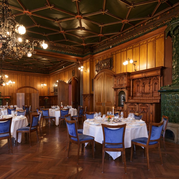 Elegantes Restaurant mit Holzmöbeln und runden Tischen, grüne Kachelofenwand.