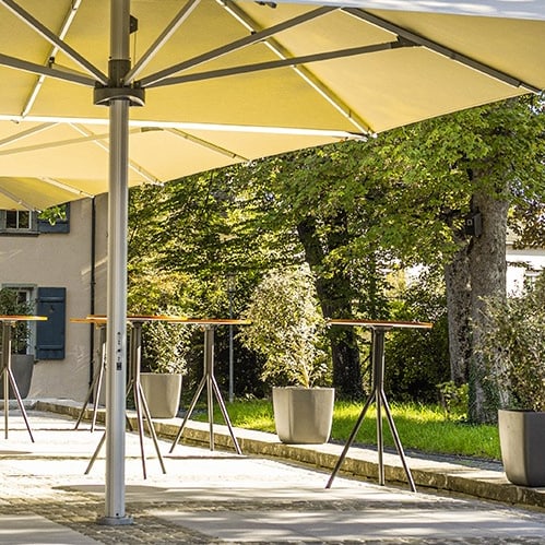 Sonnenschirme auf Terrasse mit Bäumen und Gebäude im Hintergrund.