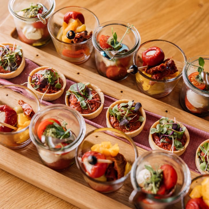 Holztablett mit Gläsern und Canapés auf einem Tisch.