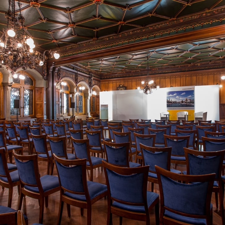 Historischer Konferenzraum mit Stuhlreihen und Bühne.